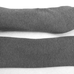 Op de afbeelding: Een paar grijze armwarmers gemaakt van een zachte, rekbare stof. De armwarmers worden getoond gevouwen en uitgevouwen.