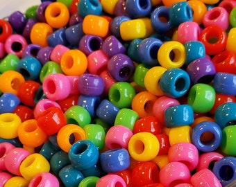 Puede incluir: Primer plano de un frasco lleno de cuentas de plástico de colores. Las cuentas son redondas y tienen un agujero en el centro. Los colores de las cuentas incluyen rojo, naranja, amarillo, verde, azul, morado y rosa.