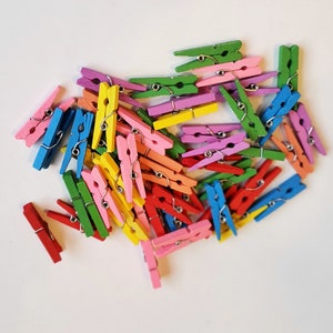 May include: A large pile of colourful wooden clothes pegs. The clothes pegs are in various shades of pink, blue, green, yellow, and red.