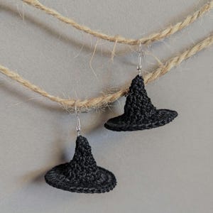 May include: A pair of black crocheted witch hat earrings hanging from a twine string.