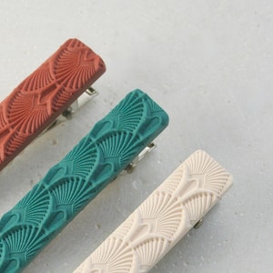 May include: Three hair clips with a decorative fan pattern. The clips are in shades of terracotta, teal, and cream.