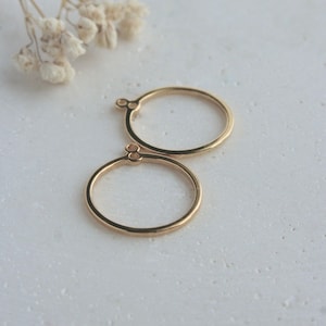 May include: Two gold rings with a small circle detail on the side. The rings are on a white surface.