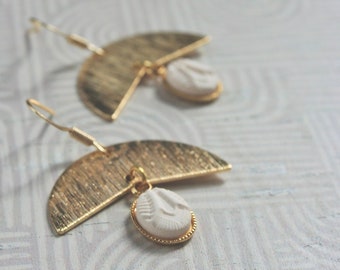 May include: A pair of gold earrings with a half-circle design and a white ceramic pendant. The pendant has a raised design.