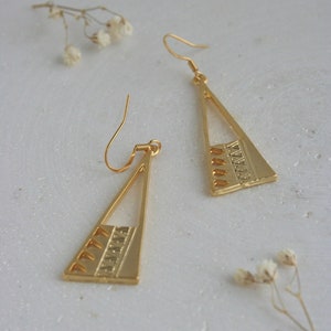 May include: A pair of gold triangle earrings with a geometric pattern. The earrings have a hook fastening.