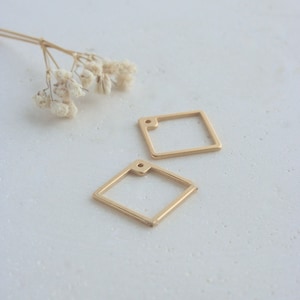 May include: Two gold-colored metal square-shaped jewelry findings with a small hole in the top corner.
