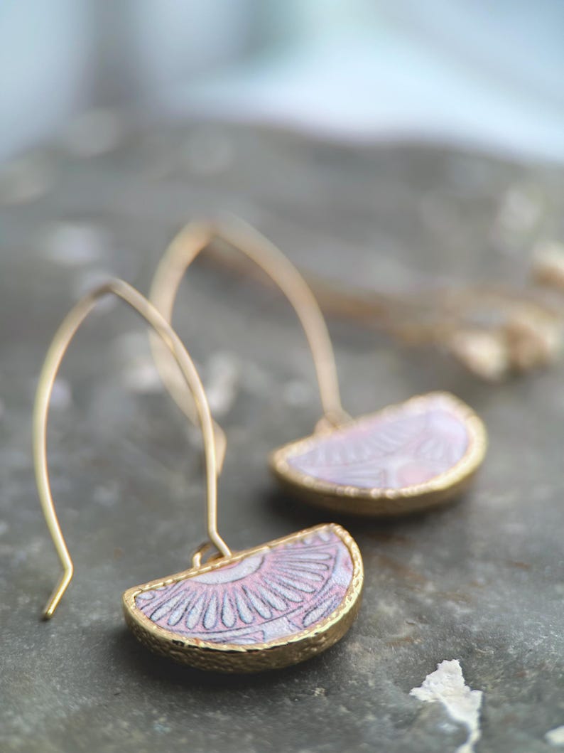 Pode incluir: Um par de brincos de argola dourados com pingentes de cer&acirc;mica de meio c&iacute;rculo rosa e branco. Os pingentes t&ecirc;m um delicado padr&atilde;o floral.