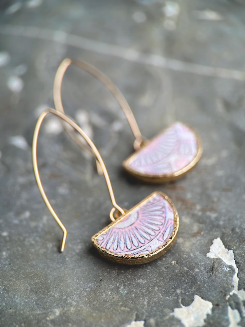 Pode incluir: Um par de brincos de ouro com pingentes de cer&acirc;mica em forma de semic&iacute;rculo com padr&atilde;o rosa e branco.