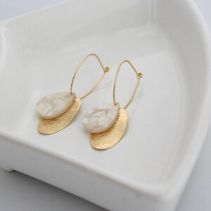 May include: A pair of gold hoop earrings with white marble-like teardrop-shaped pendants.
