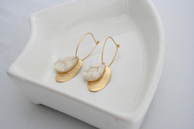 May include: A pair of gold hoop earrings with white marble-like teardrop-shaped pendants.