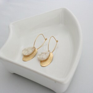 May include: A pair of gold hoop earrings with a white marbled teardrop-shaped pendant on each hoop.