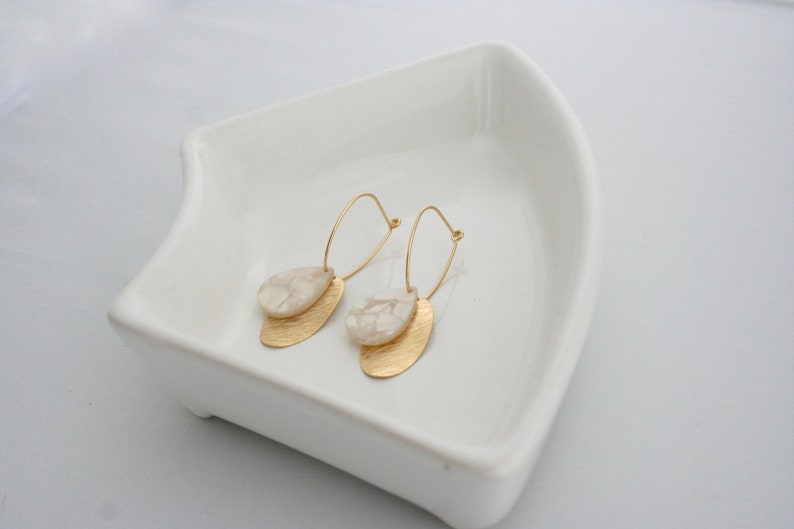 May include: A pair of gold hoop earrings with a white marbled teardrop-shaped pendant on each hoop.