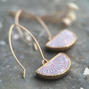 Pode incluir: Um par de brincos de argola dourados com pingentes de meio c&iacute;rculo com padr&atilde;o rosa e branco.