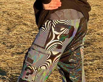May include: Black and white iridescent pants with a swirling pattern and a black pocket on the left leg. The pants have a reflective, glittery finish.