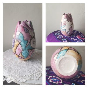 May include: A ceramic vase with a unique abstract design in shades of pink, blue, yellow, and white. The vase is shaped like a tulip and has a wide opening at the top.