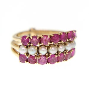 May include: A gold ring with three rows of gemstones. The top and bottom rows feature vibrant red rubies, while the middle row showcases lustrous white pearls. The ring has a classic, elegant design.