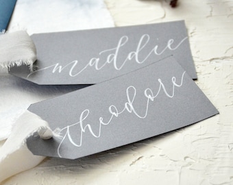 May include: Two grey paper tags with white calligraphy. The top tag says "maddie" and the bottom tag says "theodore".