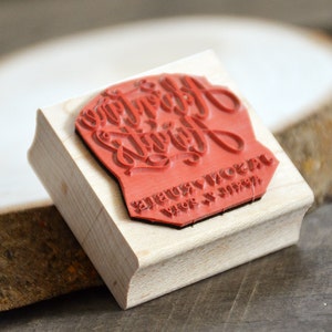 Puede incluir: Sello de madera con una superficie de goma roja. El sello dice "Happy Everything" en una fuente de escritura decorativa. El texto "JEUX & NOEL" tambi&eacute;n es visible en el sello.