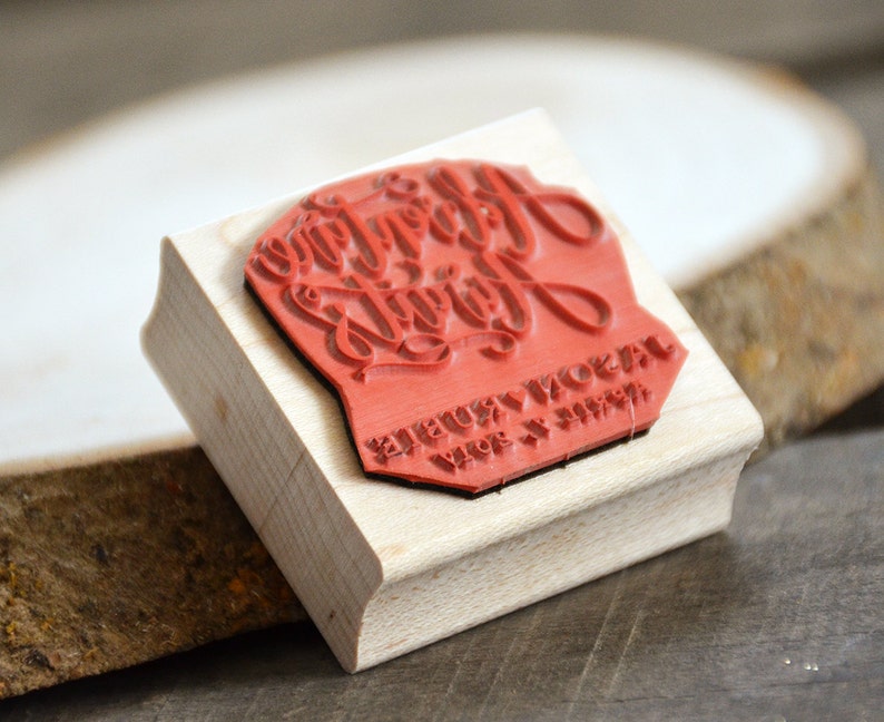 Puede incluir: Sello de madera con una superficie de goma roja. El sello dice "Happy Everything" en una fuente de escritura decorativa. El texto "JEUX & NOEL" tambi&eacute;n es visible en el sello.