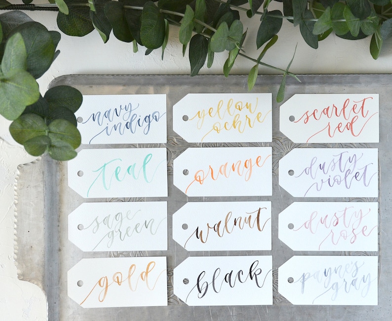 Puede incluir: Doce etiquetas blancas con nombres de colores escritos a mano en varios tonos de tinta. Los colores incluyen azul &iacute;ndigo, verde azulado, verde salvia, dorado, negro, ocre amarillo, naranja, rojo escarlata, violeta polvoriento, rosa polvoriento y gris Payne.