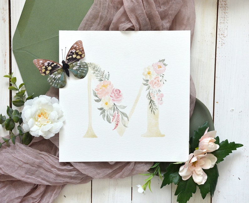 May include: Watercolor painting of the letter M decorated with pink and white flowers and green leaves. A butterfly is in the upper left corner of the image.
