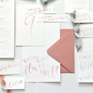 Puede incluir: Un conjunto de tarjetas y sobres relacionados con la boda con caligraf&iacute;a en tonos rosa y gris. Las tarjetas incluyen un men&uacute;, un n&uacute;mero de mesa, una solicitud de dama de honor y una solicitud de dama de honor. El texto en las tarjetas incluye "&iquest;Quieres ser mi dama de honor?" y "Para mis damas de honor".