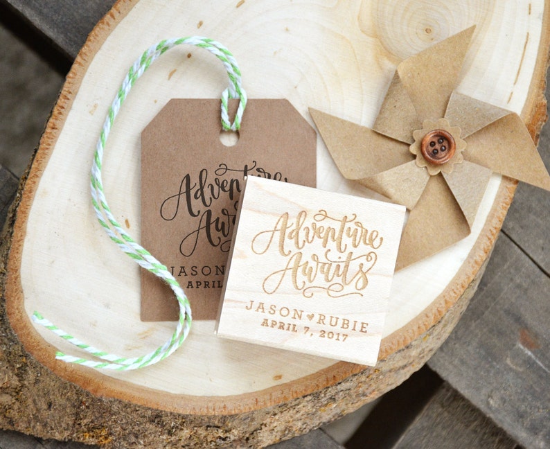 Puede incluir: Un letrero de madera con el texto "Adventure Awaits" en escritura cursiva. El letrero est&aacute; personalizado con los nombres "Jason & Rubie" y la fecha "April 7, 2017".