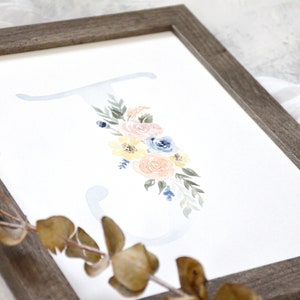 May include: A watercolor painting of the letter "J" with a floral design. The flowers are in shades of pink, yellow, and blue. The background is a light blue.