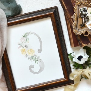 May include: A watercolor painting of a floral arrangement with yellow and pink flowers, and green leaves, surrounding a gray number three in a brown frame.