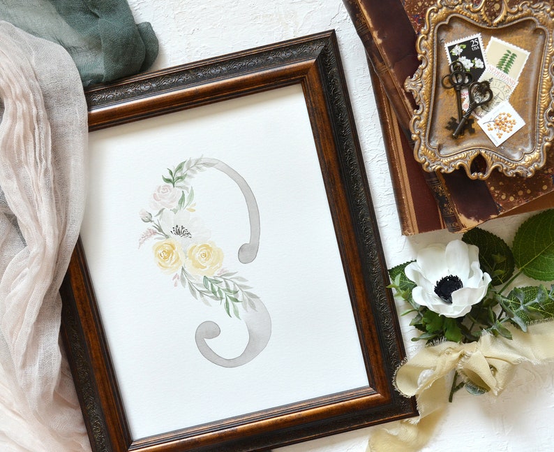 May include: A watercolor painting of a floral arrangement with yellow and pink flowers, and green leaves, surrounding a gray number three in a brown frame.
