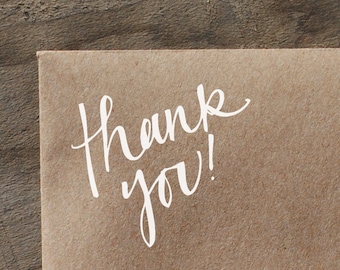 May include: A brown paper envelope with the handwritten message "Thank you!" in white ink.