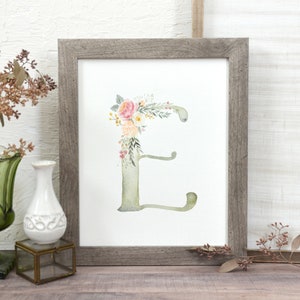 May include: A framed watercolor print of the letter "E" decorated with pink, yellow, and green floral elements.
