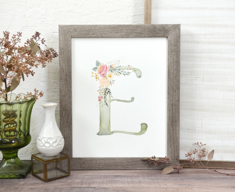 May include: A framed watercolor print of the letter "E" decorated with pink, yellow, and green floral elements.