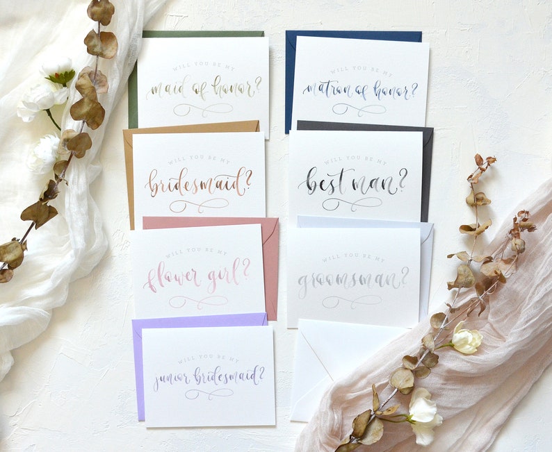 May include: Set of eight cards with different wedding party titles, including maid of honor, matron of honor, bridesmaid, best man, groomsman, flower girl, and junior bridesmaid. The cards are printed on white cardstock with calligraphy-style lettering.