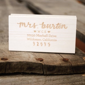 Puede incluir: Sellos de dirección de devolución de madera blanca con el texto "mrs. burton" y "WCE" con dos corazones, seguido de la dirección "20150 Mayhall Drive, Wildomar, California 92595".