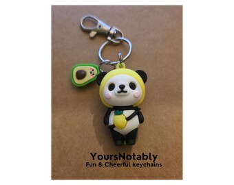 May include: A novelty keychain featuring a panda bear wearing a yellow hood and holding a pineapple. The keychain also includes an avocado charm. The text "YoursNotably Fun & Cheerful keychains" is visible.