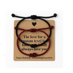 May include: Two adjustable friendship bracelets, one black and one burgundy, are displayed on a brown card. The card has a black heart and the text "The love for a custom text] last forever, I will always love you."