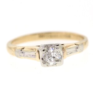 May include: A gold and white engagement ring with a single round diamond in the center and two smaller diamonds on either side.