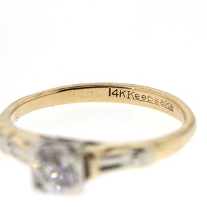 May include: A gold ring with a single diamond and two smaller diamonds on the band. The ring is inscribed with "14K Keepsake".