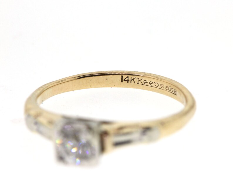 May include: A gold ring with a single diamond and two smaller diamonds on the band. The ring is inscribed with "14K Keepsake".
