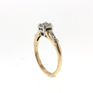 May include: A gold and white engagement ring with a single round diamond in the center and smaller diamonds on the band.
