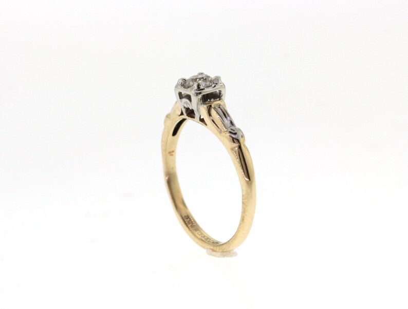 May include: A gold and white engagement ring with a single round diamond in the center and smaller diamonds on the band.