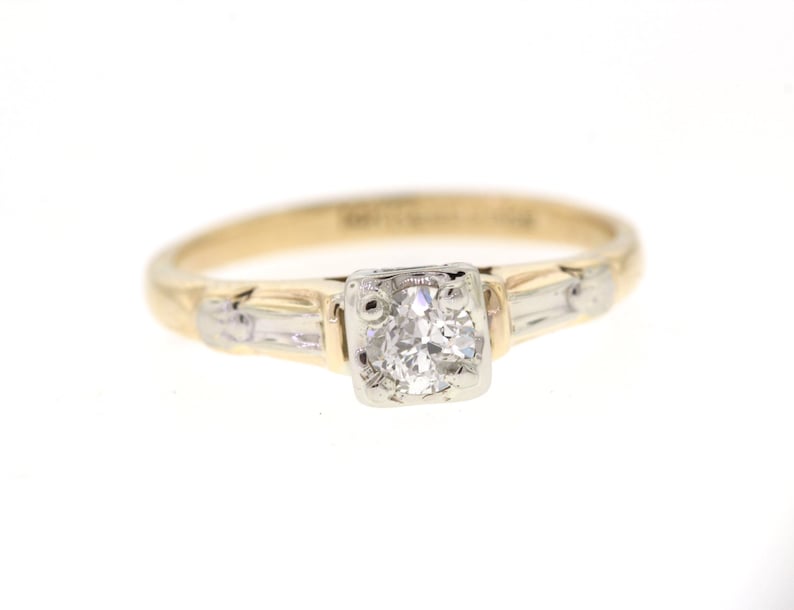 May include: A gold and white engagement ring with a single round diamond in the center and two smaller diamonds on either side.