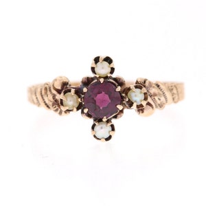 Może przedstawiać: Złoty pierścionek z czerwonym kamieniem szlachetnym otoczonym pięcioma białymi perłami.