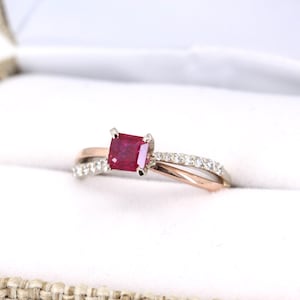 Op de afbeelding: Een ring van rosé- en witgoud met een vierkante robijn en een band met kleine diamanten.