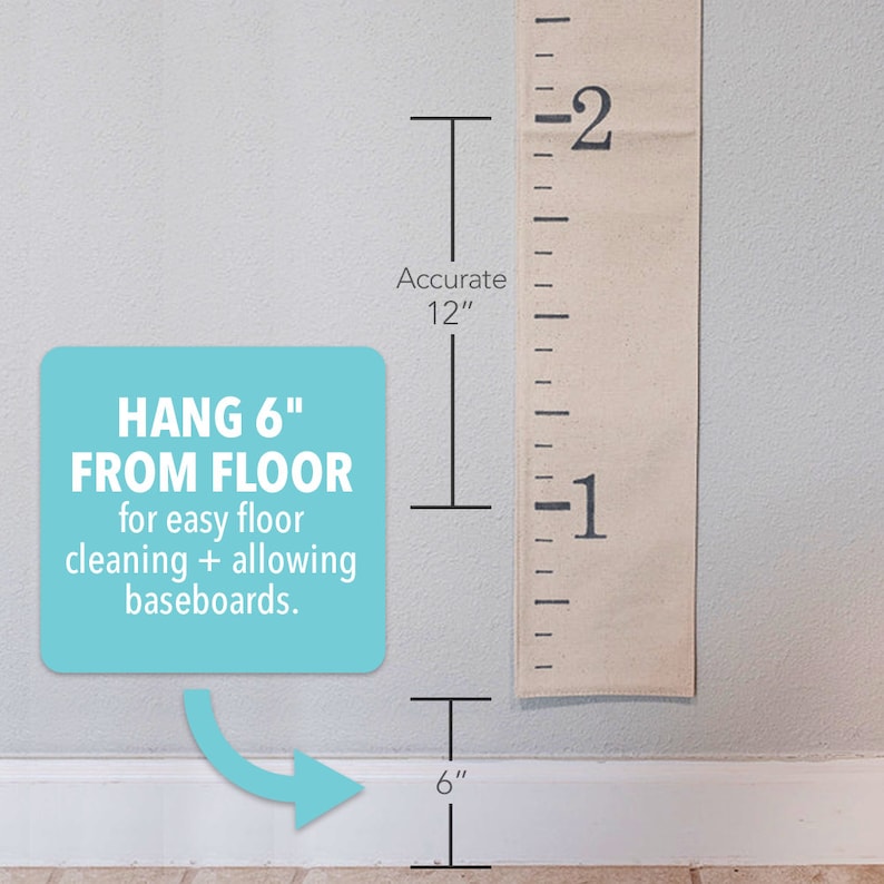 May include: A white canvas growth chart with black markings and numbers. The chart is hanging on a white wall with a white baseboard. The text "HANG 6" FROM FLOOR" is printed on a light blue square. The text "for easy floor cleaning + allowing baseboards." is printed below the first line of text. The text "Accurate 12" is printed next to the chart. The text "6" is printed below the chart.