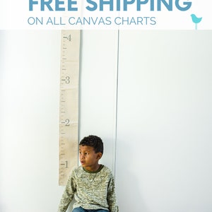 May include: A young boy sits on the floor in front of a canvas growth chart with the text "FREE SHIPPING ON ALL CANVAS CHARTS" and a blue bird icon. The chart is marked with numbers from 1 to 6.