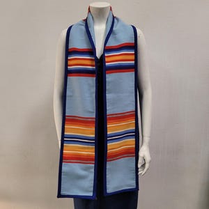 May include: A light blue scarf with a striped pattern in red, orange, yellow, and white. The scarf has a dark blue border and is displayed on a mannequin. The scarf is a graduation stole.