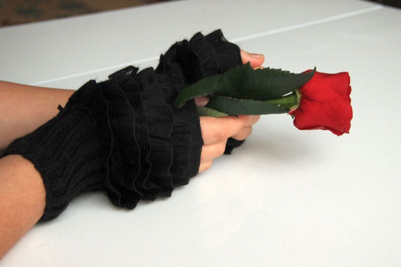 Pode incluir: Um par de luvas pretas sem dedos com babados e uma &uacute;nica rosa vermelha na m&atilde;o.