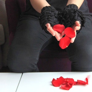 Pode incluir: Uma pessoa vestindo roupas pretas e luvas de renda pretas est&aacute; segurando p&eacute;talos de rosa vermelha em suas m&atilde;os. As p&eacute;talas est&atilde;o caindo na superf&iacute;cie branca abaixo.
