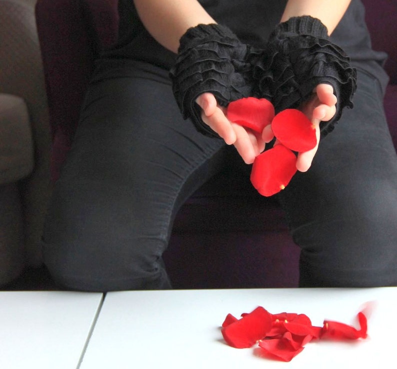 Pode incluir: Uma pessoa vestindo roupas pretas e luvas de renda pretas est&aacute; segurando p&eacute;talos de rosa vermelha em suas m&atilde;os. As p&eacute;talas est&atilde;o caindo na superf&iacute;cie branca abaixo.